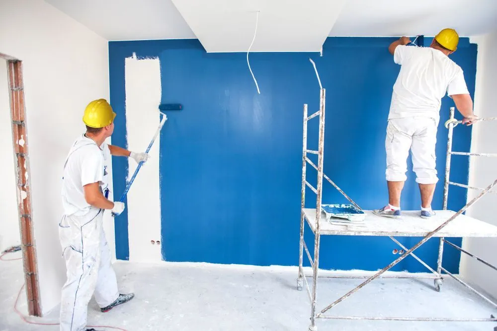 Two professional painters rolling paint onto a blue feature wall